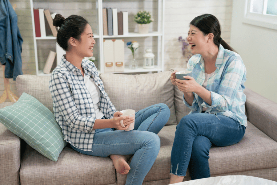 two roommates talking over coffee inside their home on the couch
